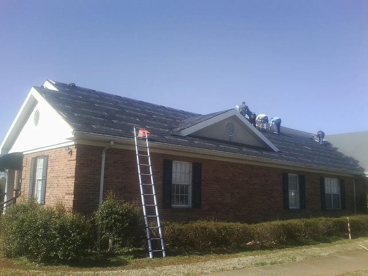 Crew tearing shingles off a brick ranch roof with a ladder set — Metal Roof Repair work by our crew in Herald
