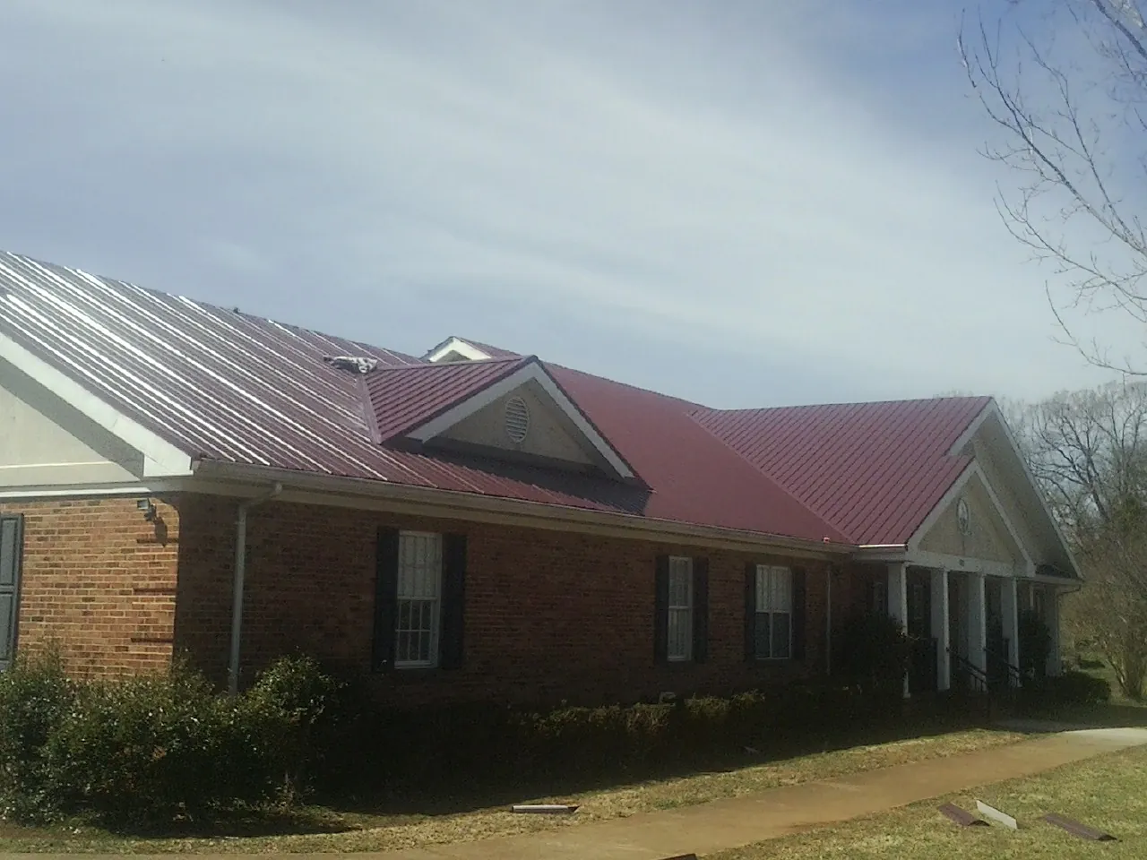 Red metal roof with gabled entries on a long brick building, from a Hail Damage Roof Repair job in Herald