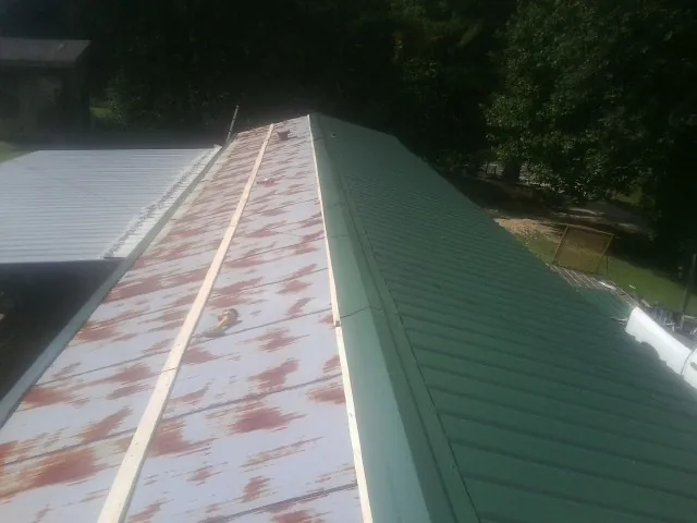 Old rusted panels beside newly installed green metal roofing — Wind Damage Roof Repair by Roofing Brothers in Herald