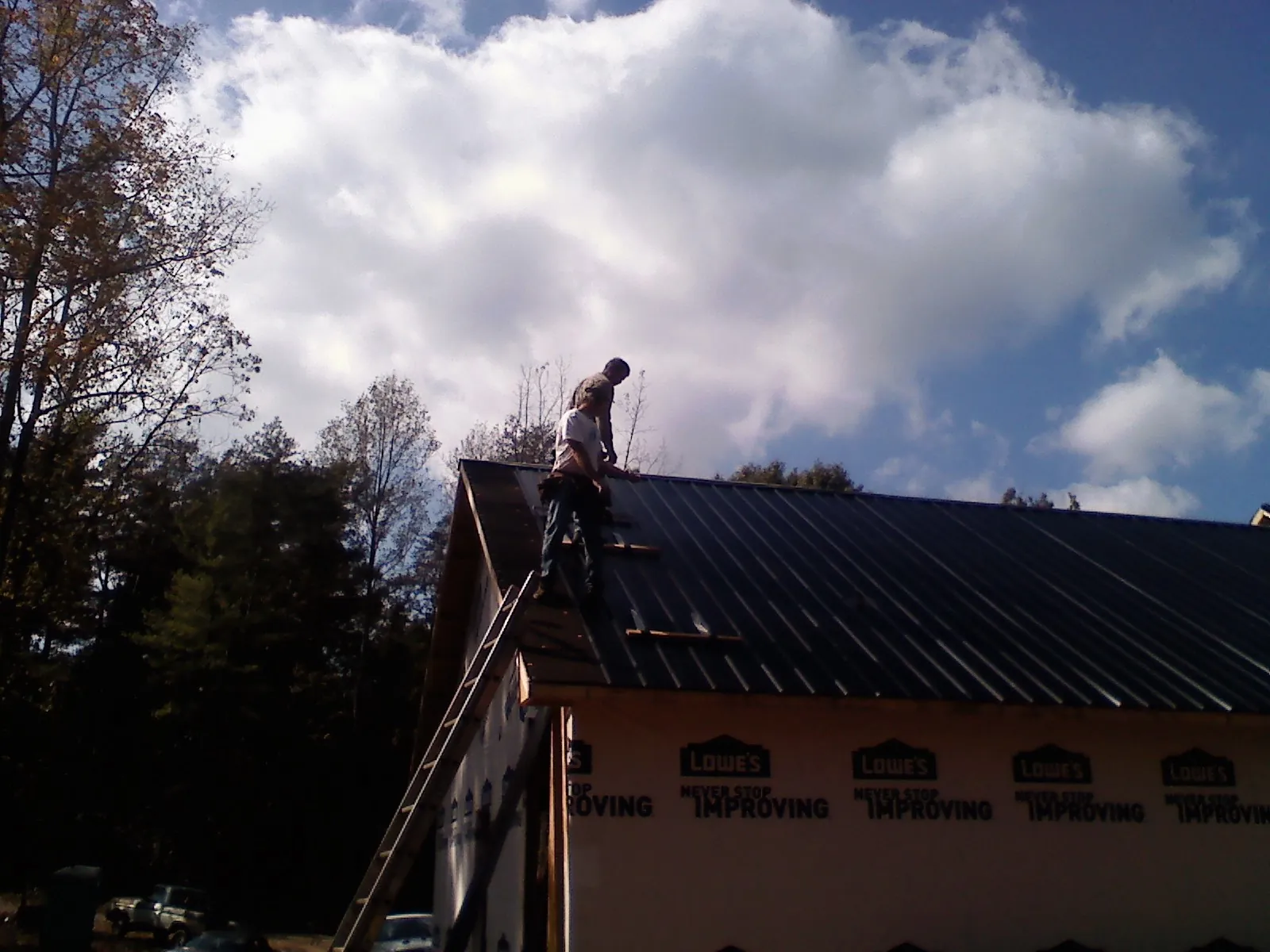 Roofer fastening dark metal panels high against a cloudy sky, from a Roof Inspection job in Herald